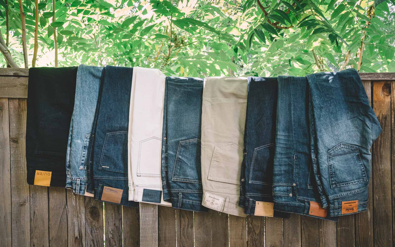 Various mens jeans draped over wooden fence