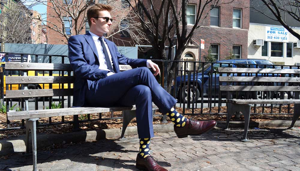 man sittin gon a bench wearing a casual blue suit and oxfords