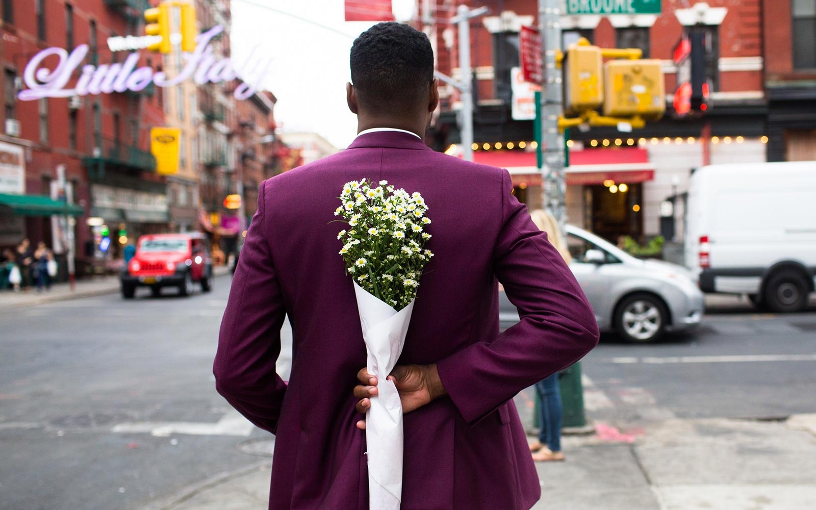 Man wearing purple suits holding flowers behind his back