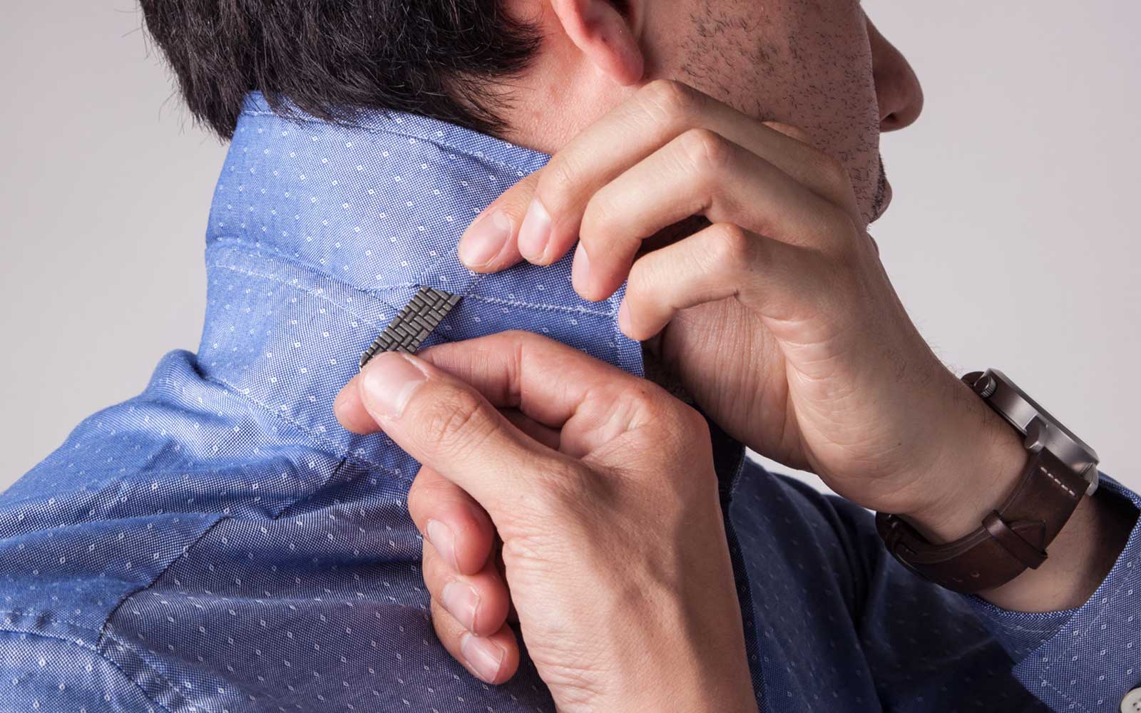 Man putting collar stay in blue shirt