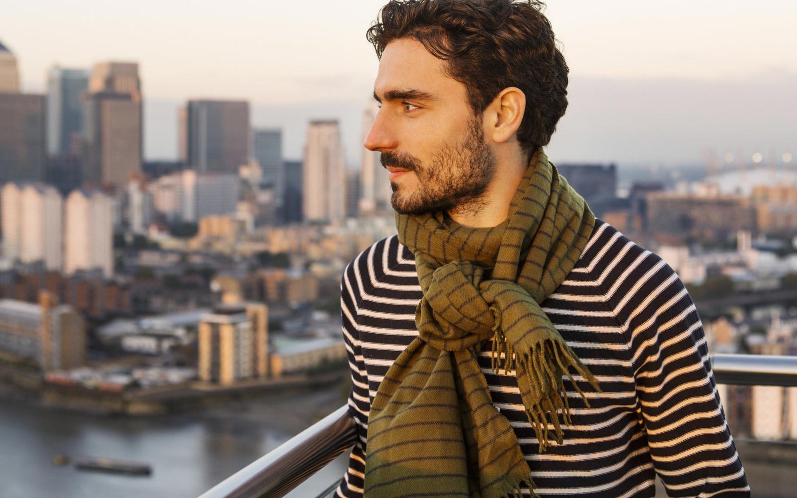 Man wearing green scarf on balcony looking at city
