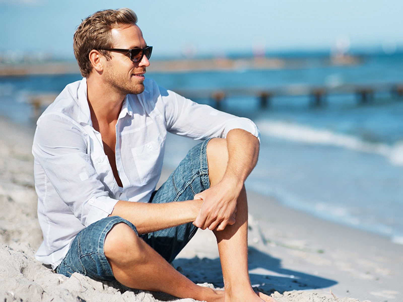 Man sitting on beach wearing button up shirt